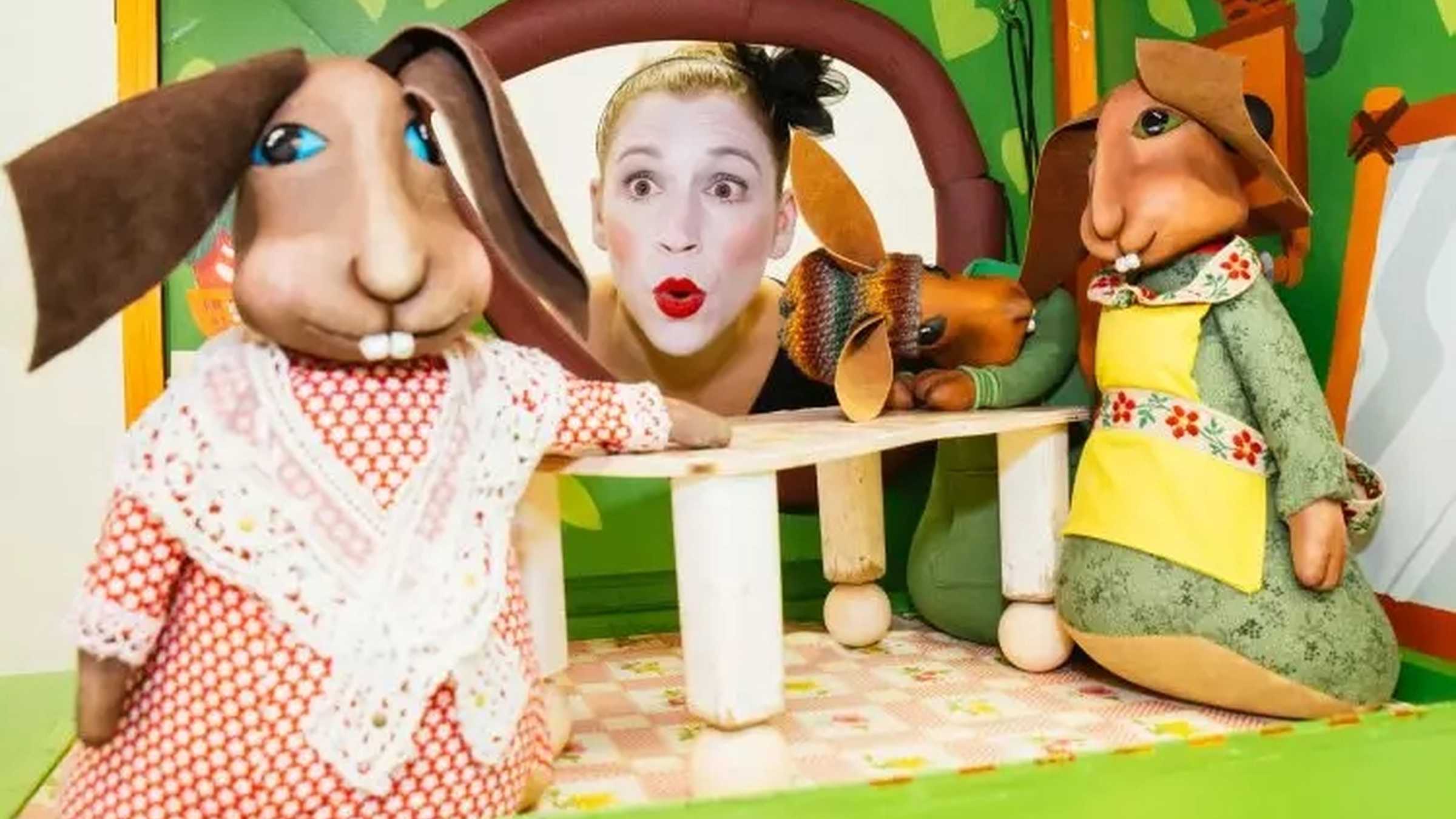 Der Sängerkrieg der Heidehasen eine Zimmerszene mit Hasenpuppen zu sehen, die Puppenspielerin Julia Raab schaut mit einem überraschten Gesichtsausdruck zu ihnen hinein.