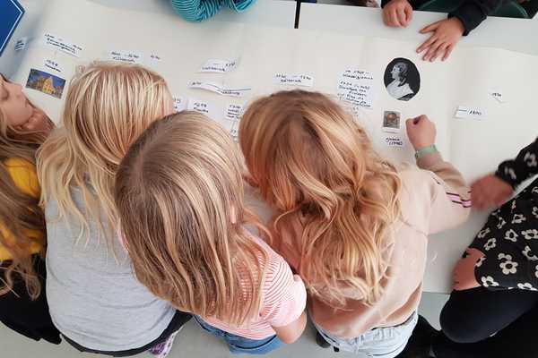 Mädchen arbeiten schreiben Texte und kleben Bilder auf eine Papierbahn