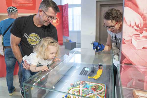 Ein kleines Mädchen Ein Vater hält seine kleine Tochter im Armen, die sich ein dredimensionales Spiel mit Autos ansieht.