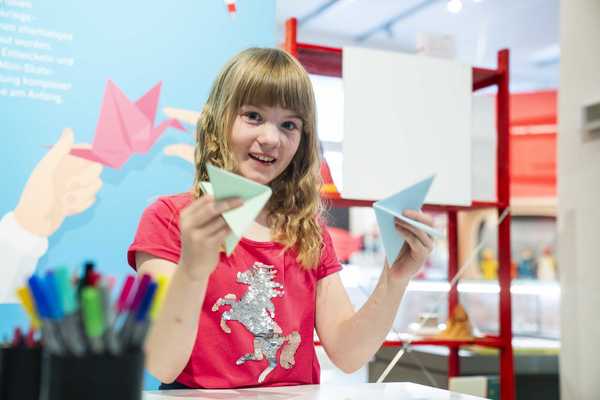 Papierspiele Ein Mädchen hält Papierspielzeug in ihren Händen und lacht.